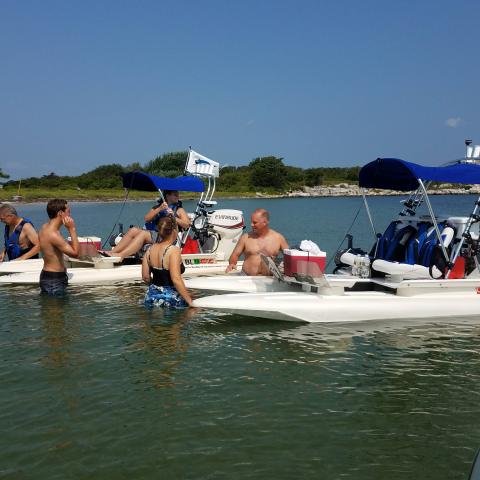Group of people standing in shallow water next to boats