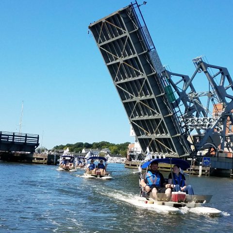 a group of people in a boat on a body of water with Bascule bridge in the background